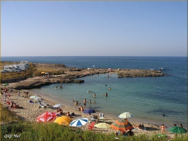 Caletta sabbiosa di Egnazia–Case Bianche con scogli, ombrelloni e mare calmo a Savelletri.