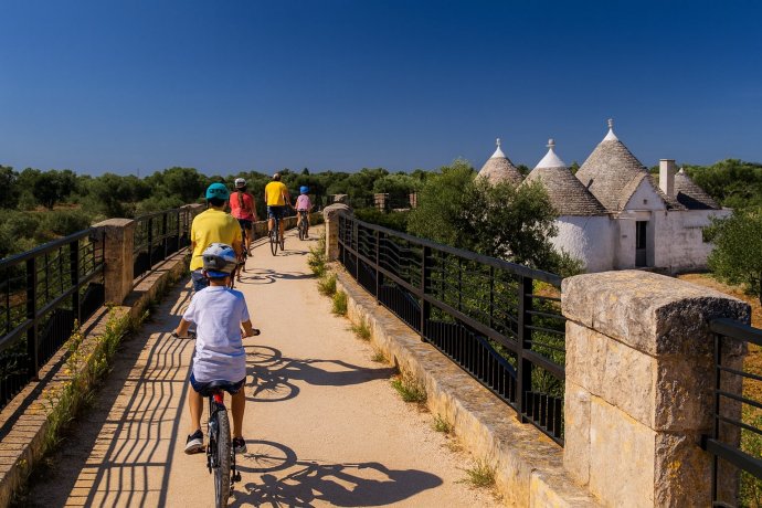 Ciclisti su ponte della Ciclovia AQP accanto a trulli e ulivi