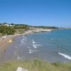 Una spiaggia sabbiosa con mare azzurro e colline verdi sullo sfondo.