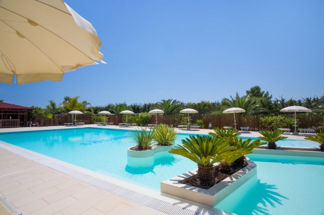 Piscina luminosa con palme e ombrelloni.