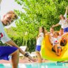 Persone sorridenti su uno scivolo giallo vicino a una piscina.