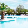 Donna in bikini sotto una palma su una piattaforma in piscina, con ombrelloni e sdraio.