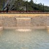 Piscina con cascata su muro di pietra.