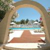 Arco in pietra con vasi che conduce a una piscina con lettini e ombrelloni in una giornata di sole.