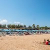 Spiaggia affollata con lettini e ombrelloni blu, cielo limpido e alcune persone sulla sabbia.