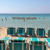 Sedie a sdraio vuote davanti al mare con bagnanti in acqua.