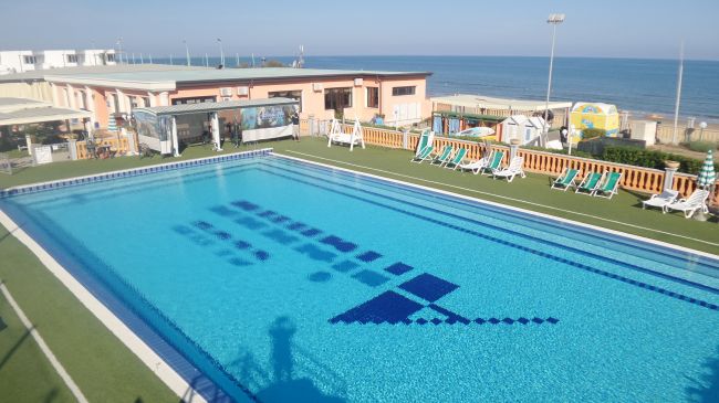 Piscina all'aperto vicino al mare con lettini.