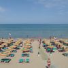 Spiaggia con ombrelloni arancioni e verdi, mare sullo sfondo.