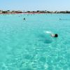 Mare azzurro con persone che nuotano e una spiaggia in lontananza.
