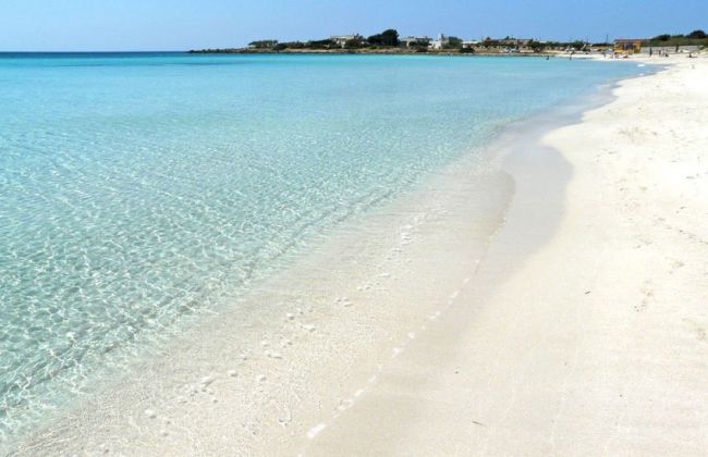 Una spiaggia di sabbia bianca con mare turchese e limpido sotto un cielo azzurro.