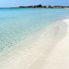 Una spiaggia di sabbia bianca con mare turchese e limpido sotto un cielo azzurro.