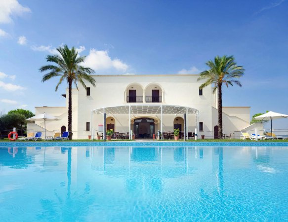 Piscina luminosa davanti a una villa bianca con palme.